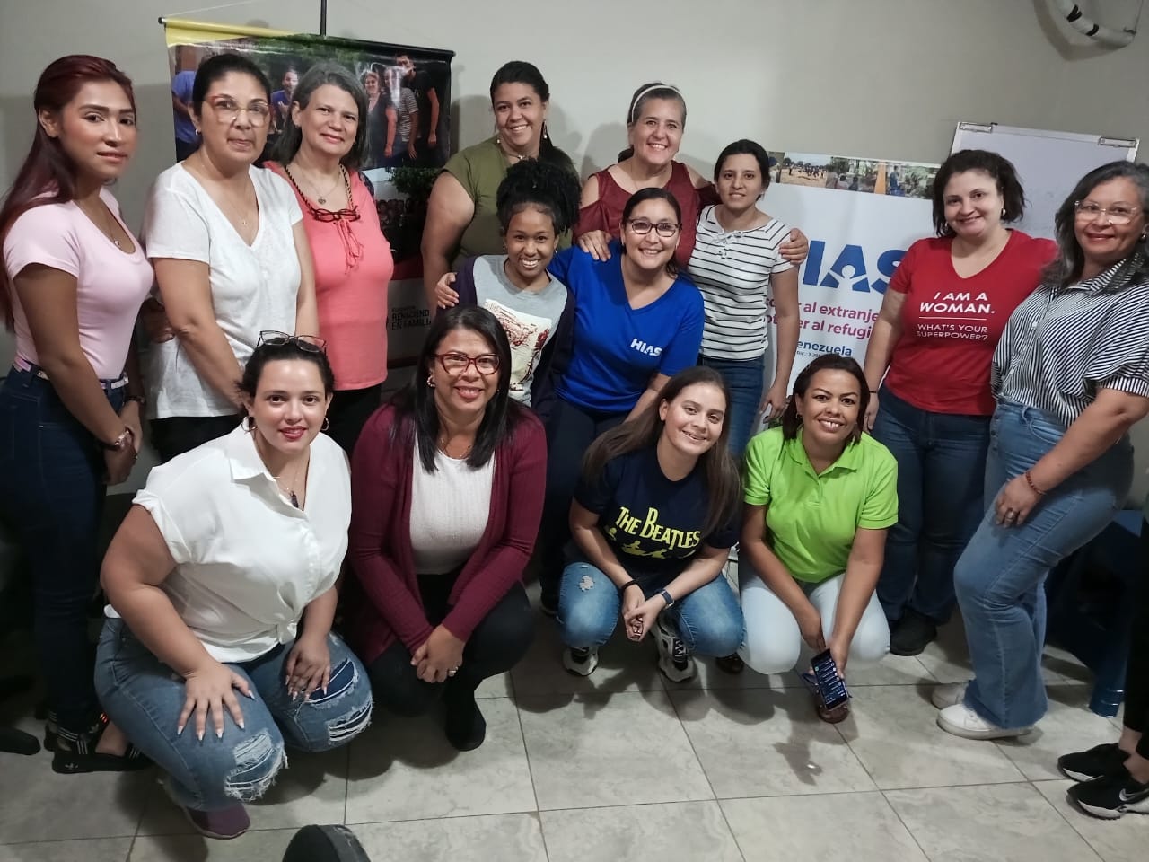 man wearing a black jacket, white shirt, blue jeans, and brown boots, playing a white electric guitar while sitting on an amp